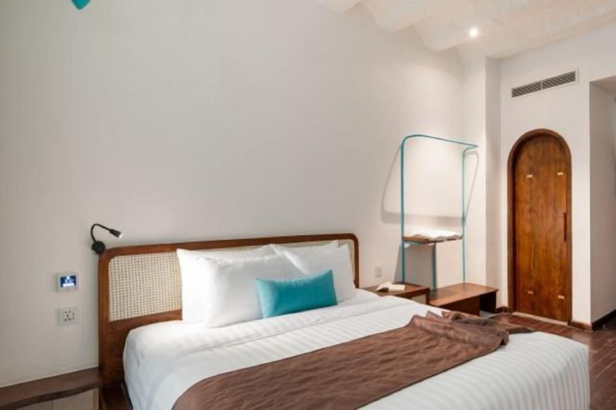 Una habitación de hotel con una cama, una mesita de noche, una lámpara y una puerta de madera.