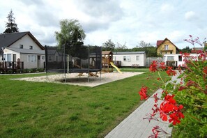 A playground with a trampoline and slide, surrounded by a grassy area and residential buildings.