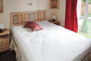 A neatly made bed with a patterned headboard, a single red pillow, and a bedside table with a lamp.