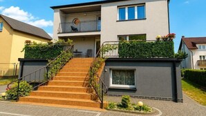 A two-story residential building with a staircase leading to a balcony, a small garden area, and a visible door. - Holiday Home near Baltic Sea & Sandy Beaches (Miedzyzdroje)