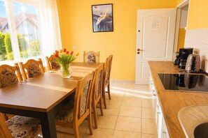 Comedor con mesa y sillas de madera, un jarrón de flores y cocina equipada con estufa y cafetera.