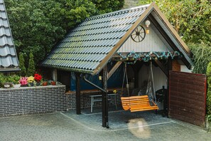 Eine kleine Holzhütte mit geneigtem Dach, einer Schaukel und einer Ziegelwand mit Blumentöpfen.