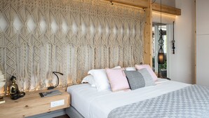 Een slaapkamer met een macramé hoofdbord, een bed met veel kussens, een nachtkastje met een lamp en een kleine Boeddhabeeld.