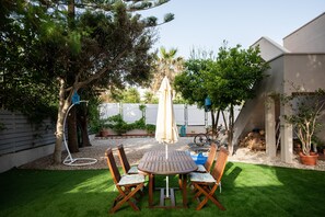 Une terrasse avec une table ronde et des chaises, entourée d’une pelouse verdoyante et d’arbres.