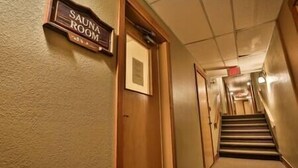 Un couloir mène à une salle de sauna dotée d’une porte en bois et d’une enseigne au-dessus.