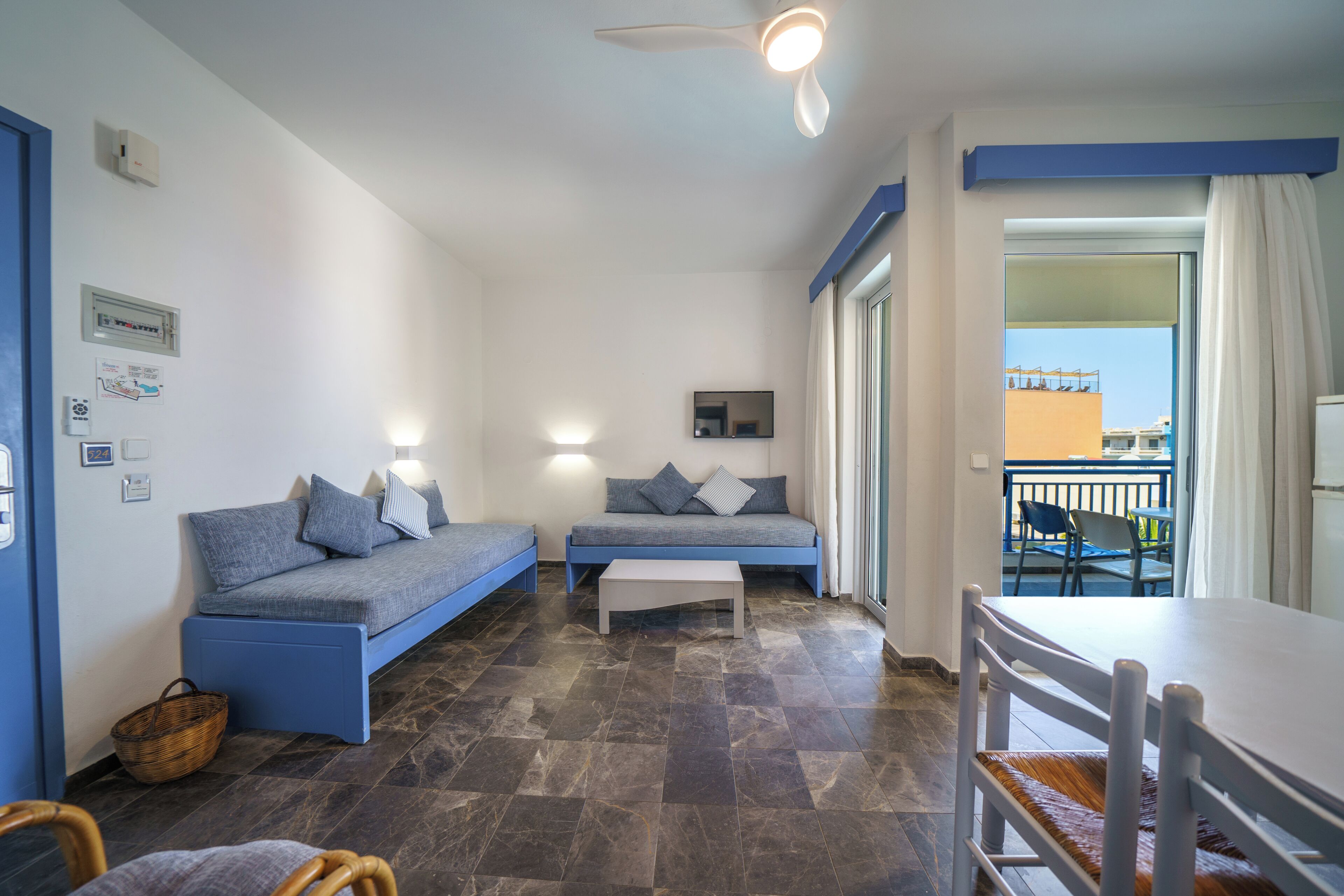 A room with a sofa, a table, and a balcony with chairs.