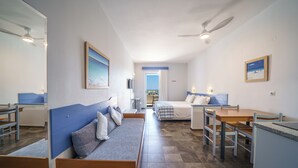 A compact hotel room with a bed, a seating area, a desk, and a view of the sea. - Ibiscos Garden Hotel (Rethymno)