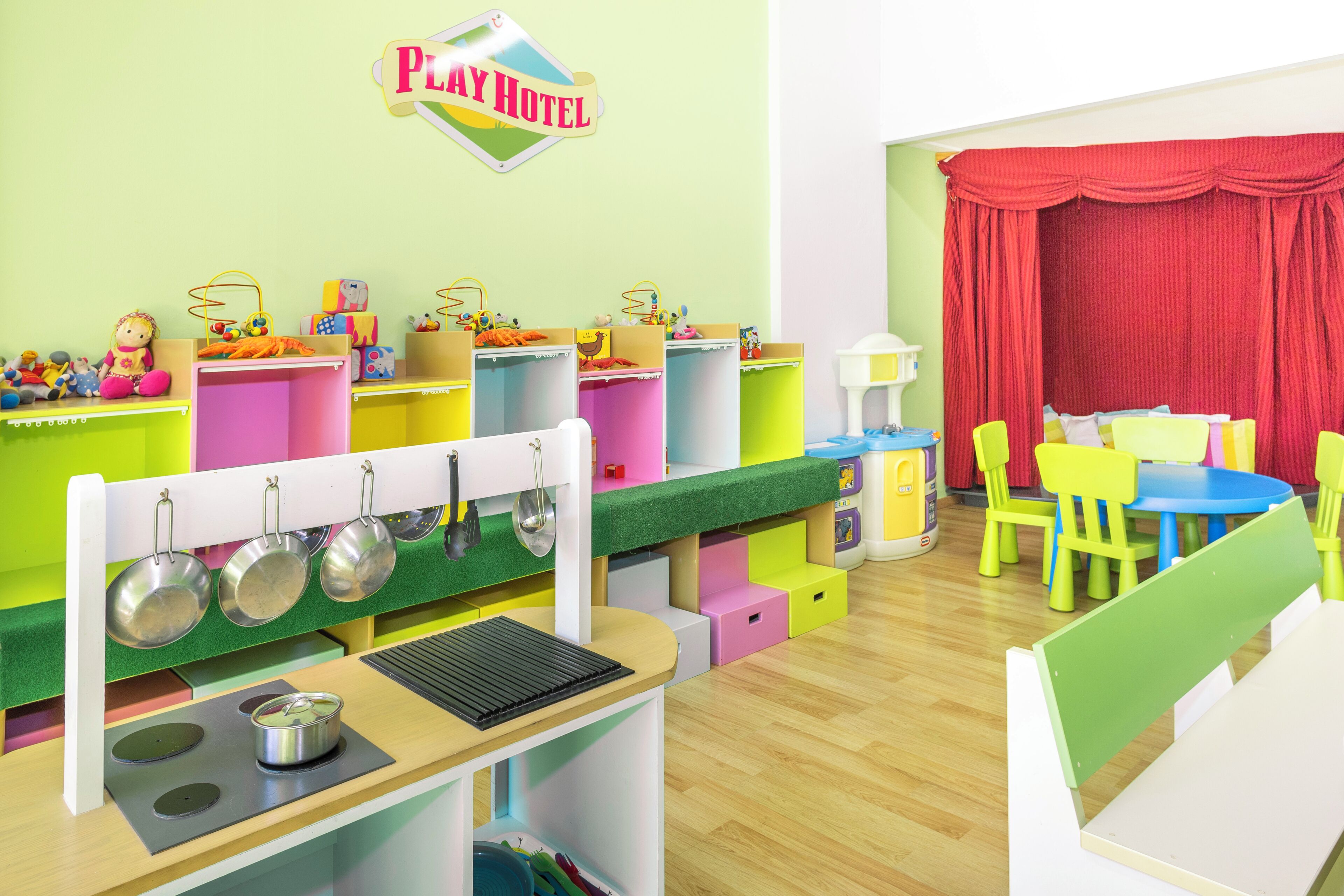 A children's play area with a Play Hotel sign, play kitchen, and colorful furniture.