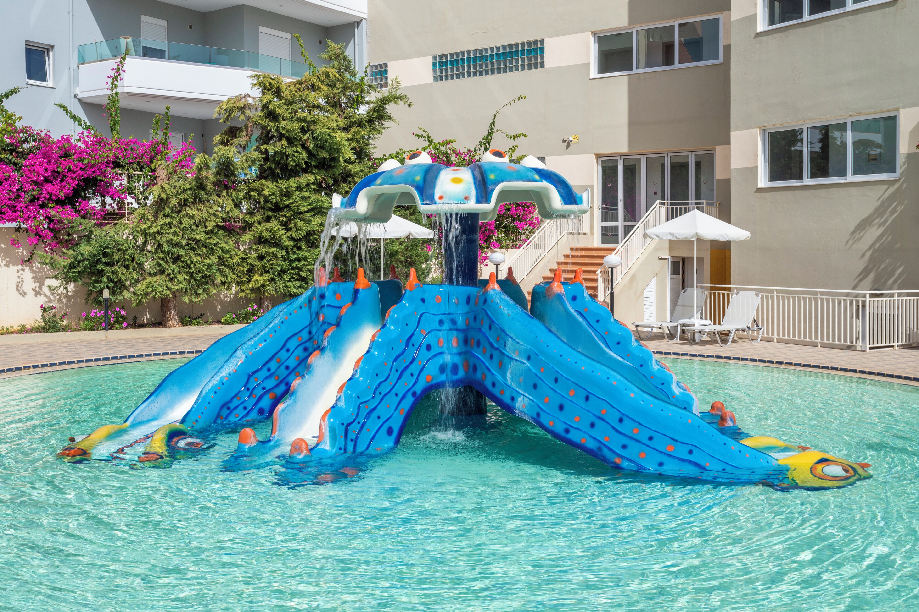 A swimming pool with a blue slide and a water fountain.