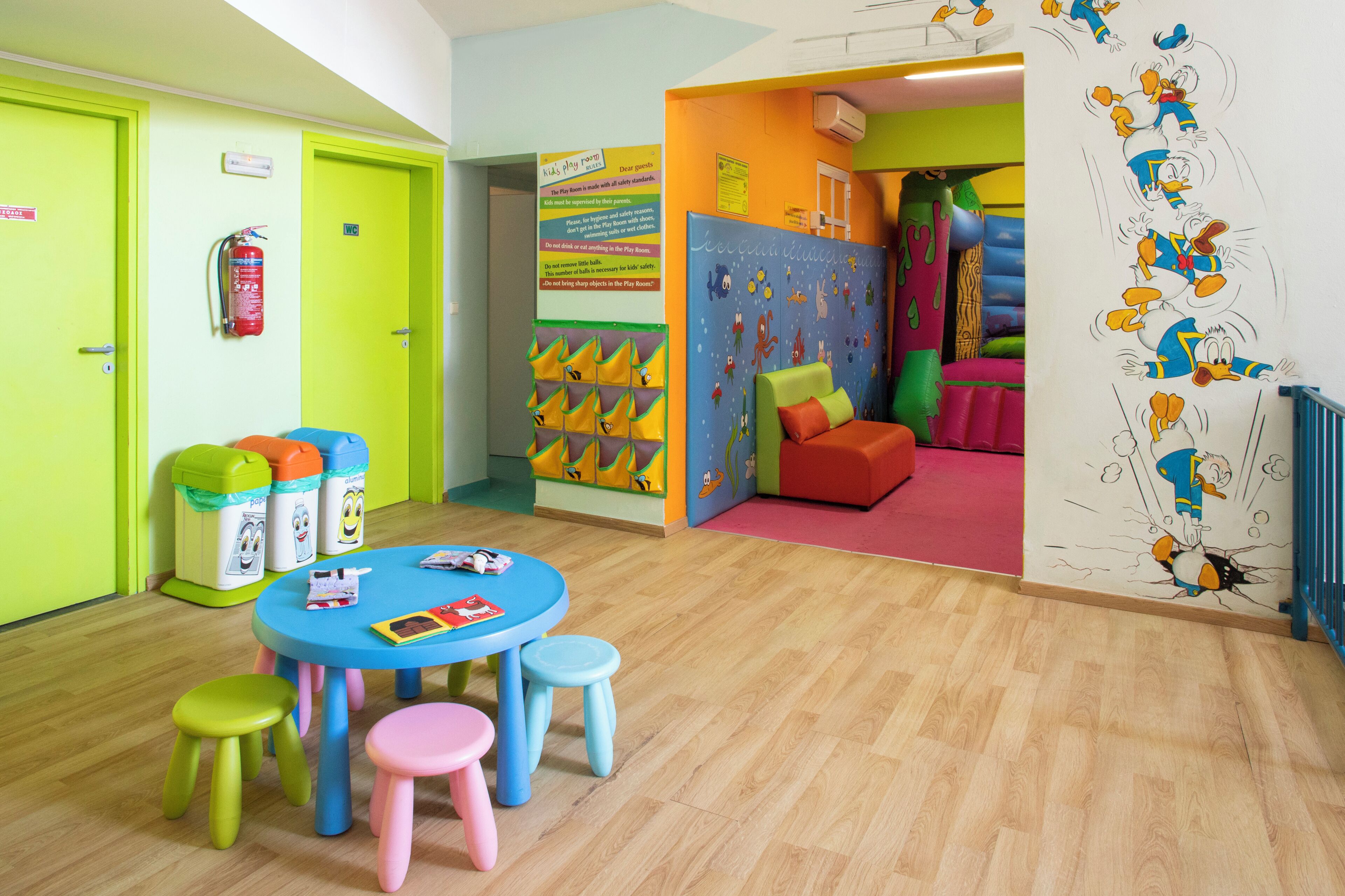 A children's playroom with a blue table, colorful stools, and a play area with a slide.