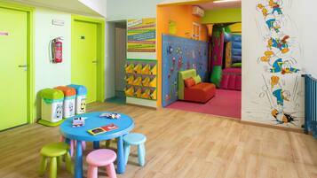 A children's playroom with a blue table, colorful stools, and a play area with a slide.