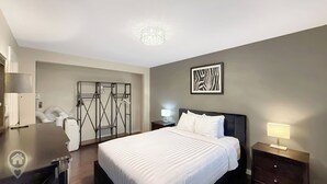 Une chambre d’hôtel comprenant un lit, des tables de chevet, une armoire, un miroir, un porte-manteau et un luminaire au plafond.