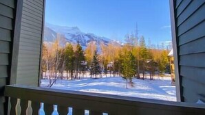 Une vue depuis une fenêtre donnant sur un paysage enneigé, avec des arbres et des montagnes.