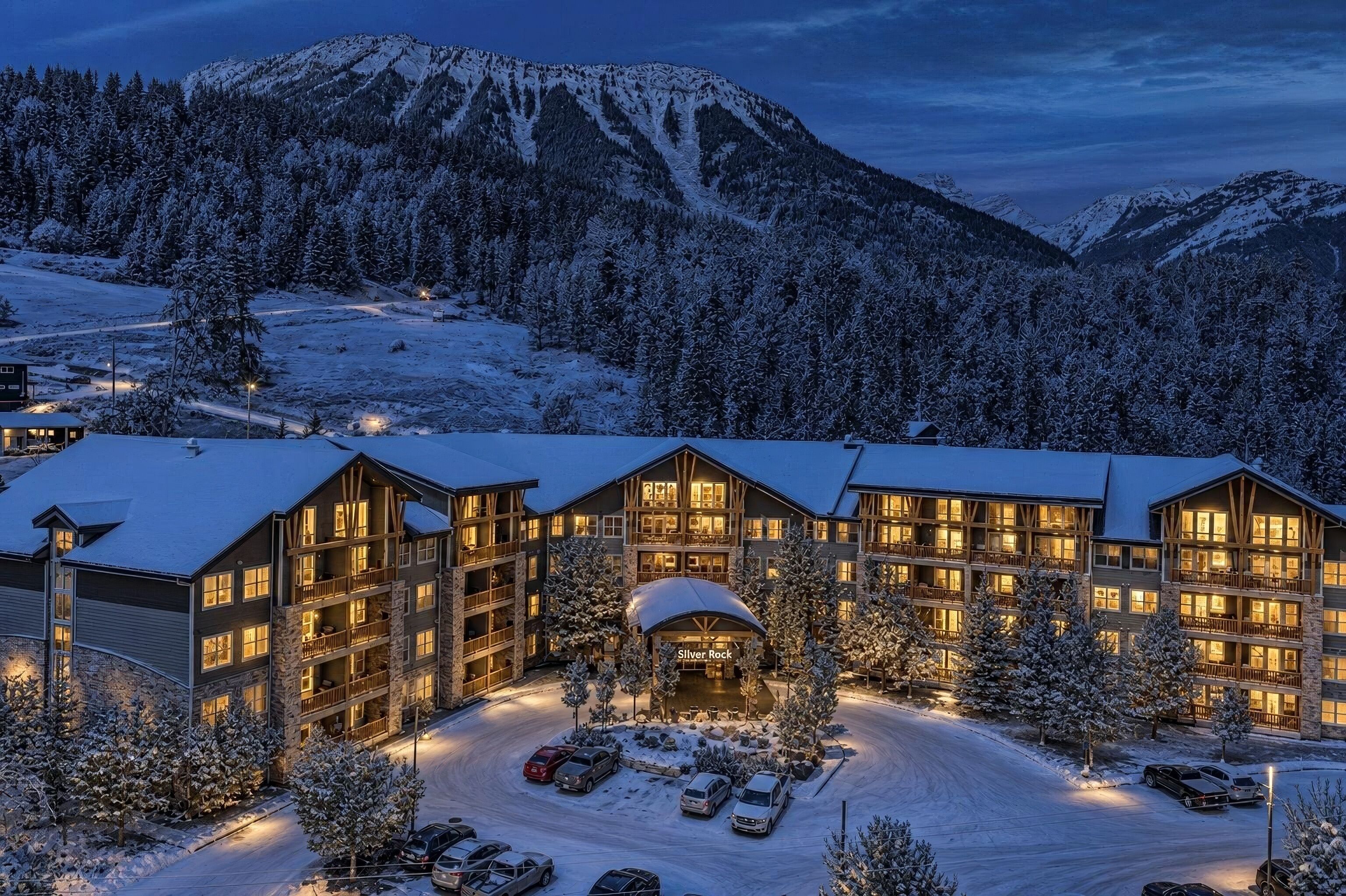 A multi-story lodge with a snow-covered landscape and mountains in the background.
