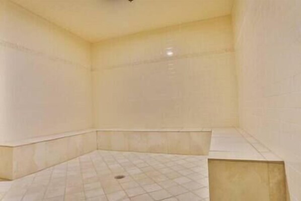 A room with a tiled floor and walls, a corner sink, and a ceiling light fixture.