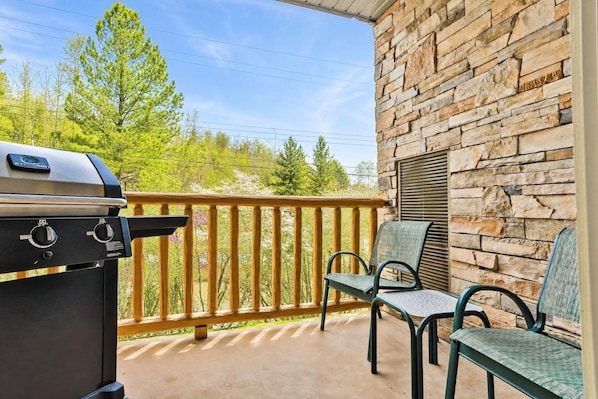 A balcony with a stone wall, a grill, and two chairs.