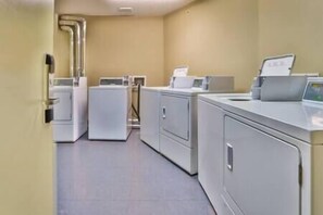 A laundry room with multiple washing machines and dryers, a control panel, and a tiled floor.