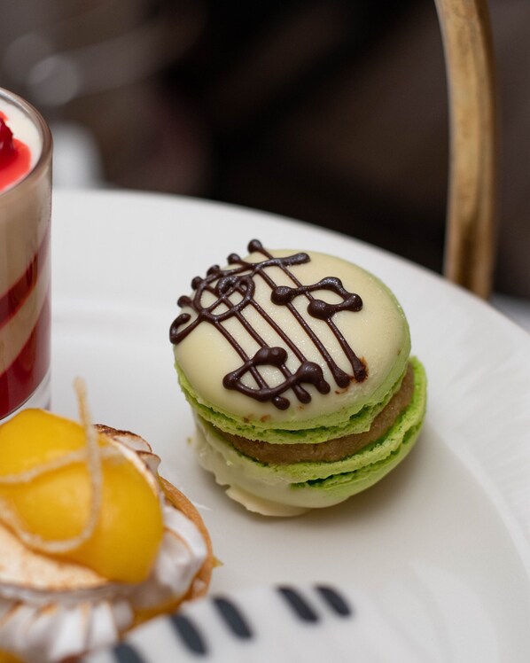 Un plato de postre con un macaron verde, una fruta amarilla y un pastel en capas.