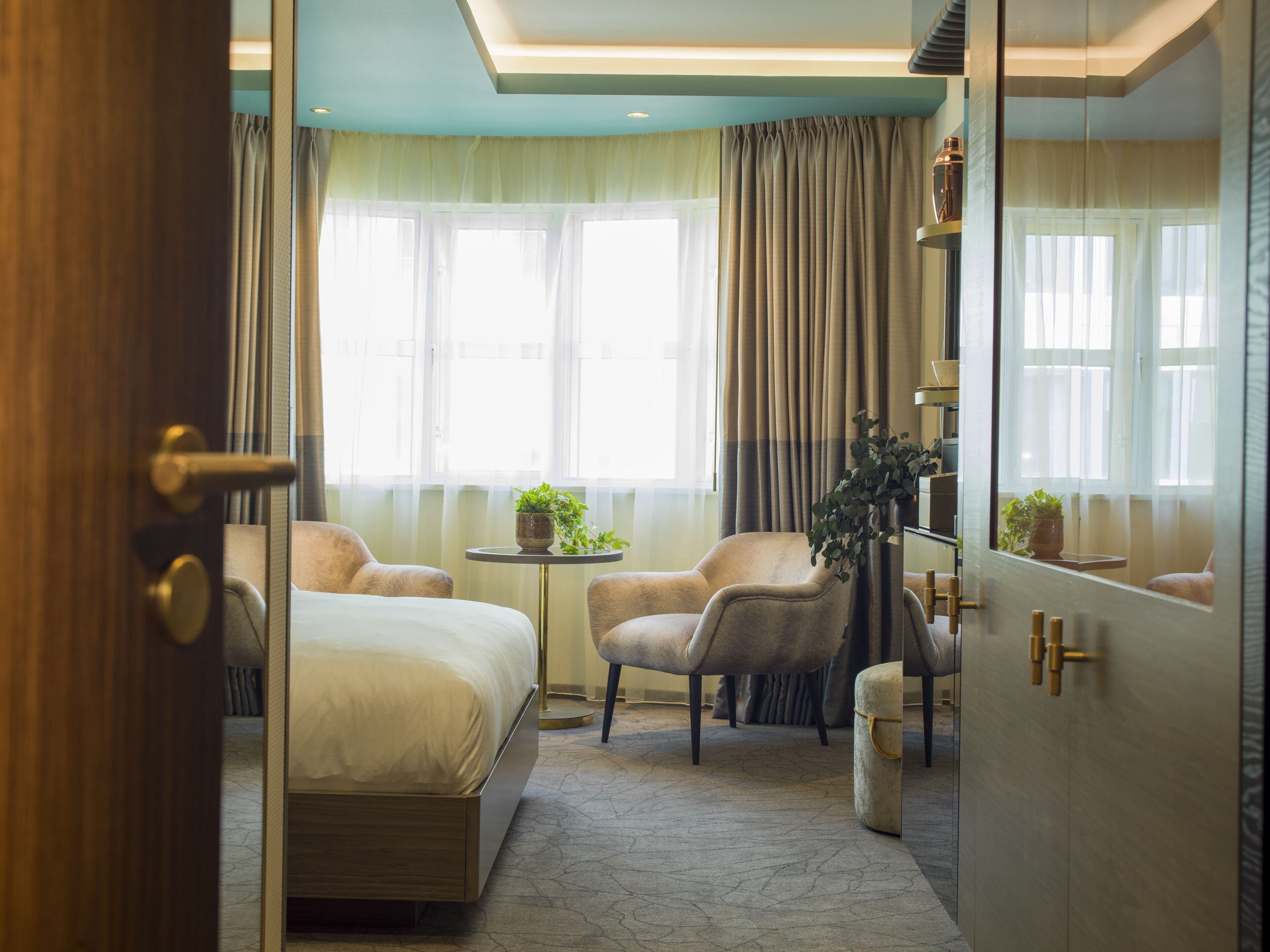 A hotel room with a bed, two armchairs, a small table, and a mirror.