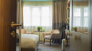 Ein Hotelzimmer mit einem Bett, zwei Sesseln, einem kleinen Tisch und einem Spiegel.