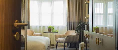 A hotel room with a bed, two armchairs, a small table, and a mirror.