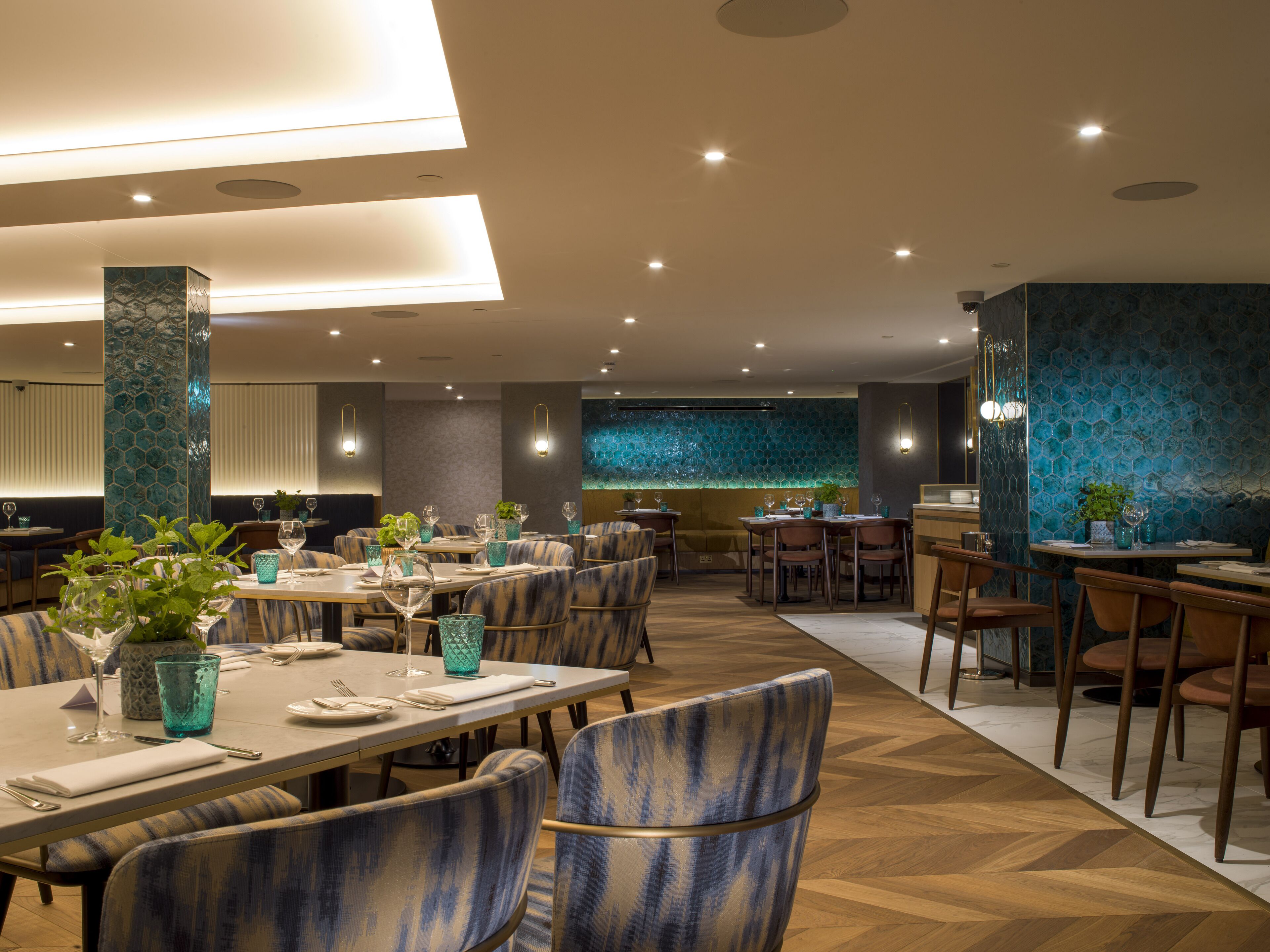 Un restaurante con varias mesas y sillas, una pared decorativa con un diseño azul y un pilar con textura.