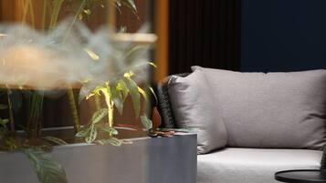Uma sala de estar moderna com um sofá cinzento, uma mesa de centro redonda e uma grande planta em vaso.