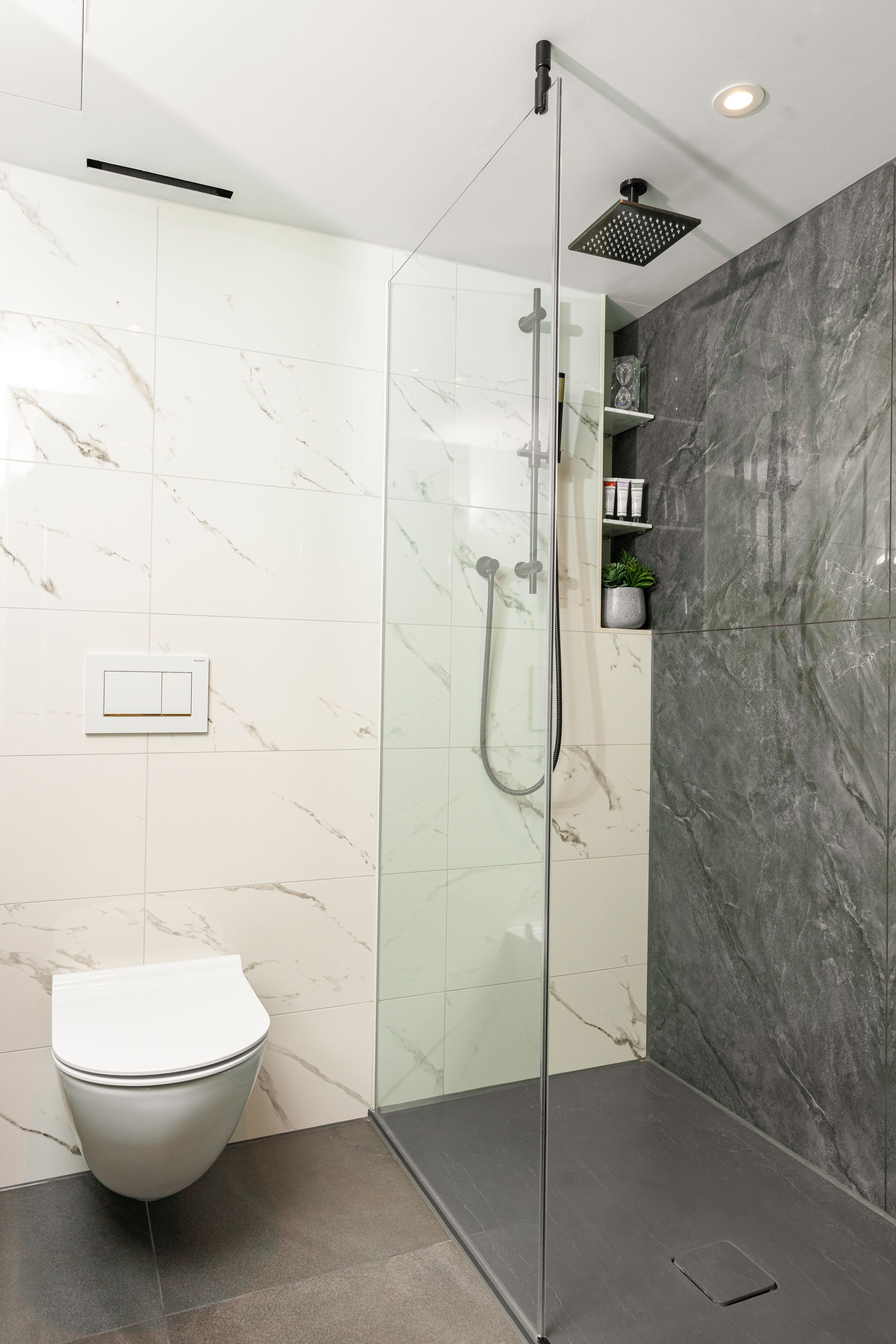 Un baño moderno con ducha acristalada, inodoro y paredes de mármol.