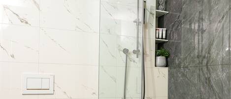Un baño moderno con ducha acristalada, inodoro y paredes de mármol.