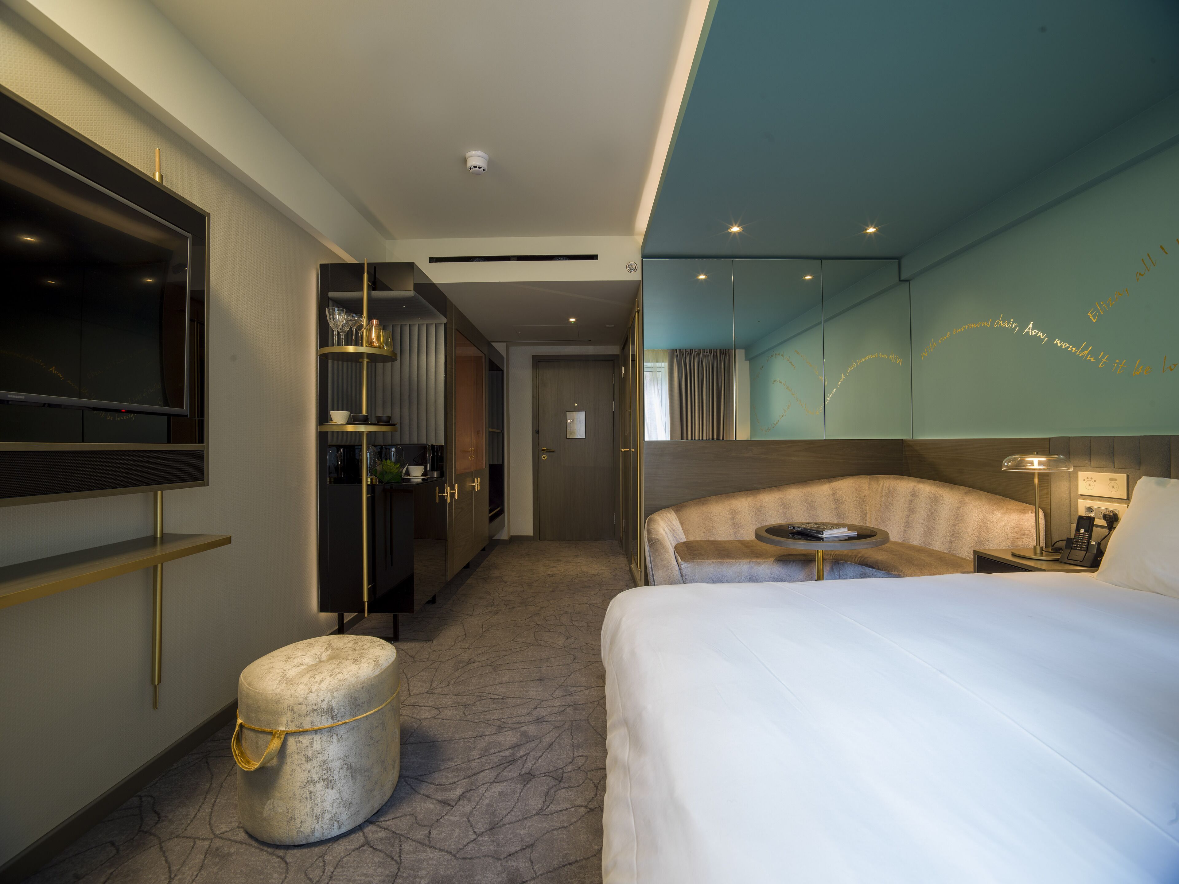 A modern hotel room with a large bed, a seating area, a TV, and a minibar.