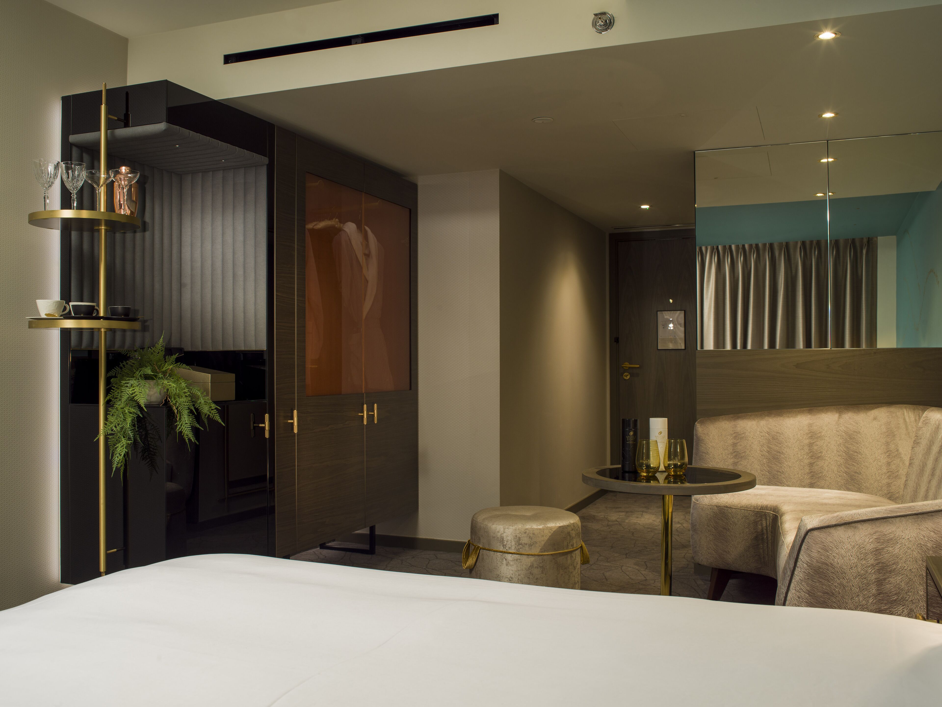 A modern hotel room with a large bed, a seating area with a small table, and a large mirror.