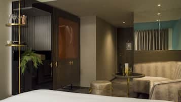 A modern hotel room with a large bed, a seating area with a small table, and a large mirror.