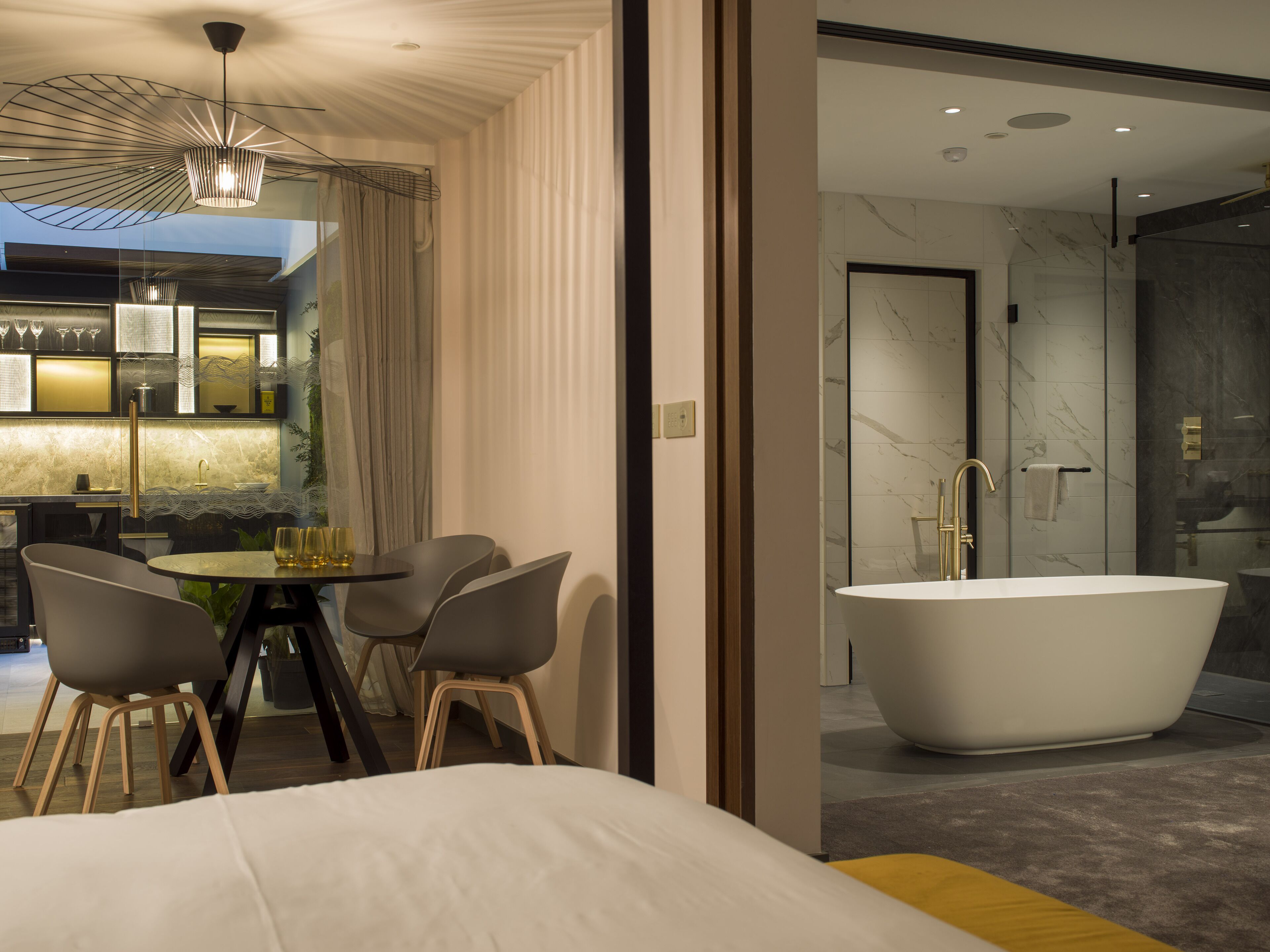 Une chambre d’hôtel moderne dotée d’un grand lit, d’un coin repas avec une table et des chaises, d’une salle de bain avec une baignoire sur pieds et offrant une vue sur le paysage urbain grâce à de grandes fenêtres.
