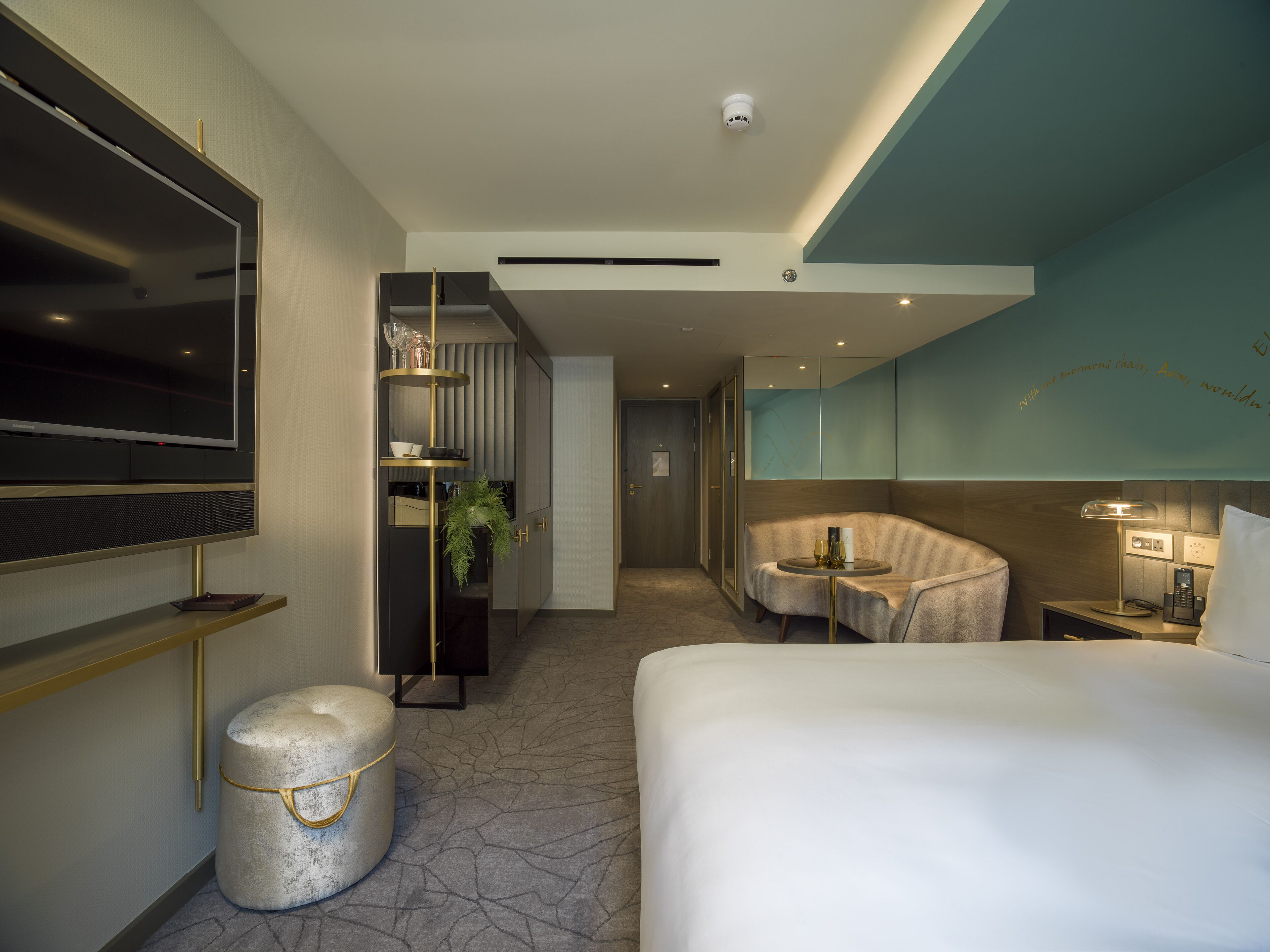 Egy modern szállodai szoba, amelyben egy nagy ágy, egy asztallal ellátott ülősarok, egy televízió és egy minibar található.