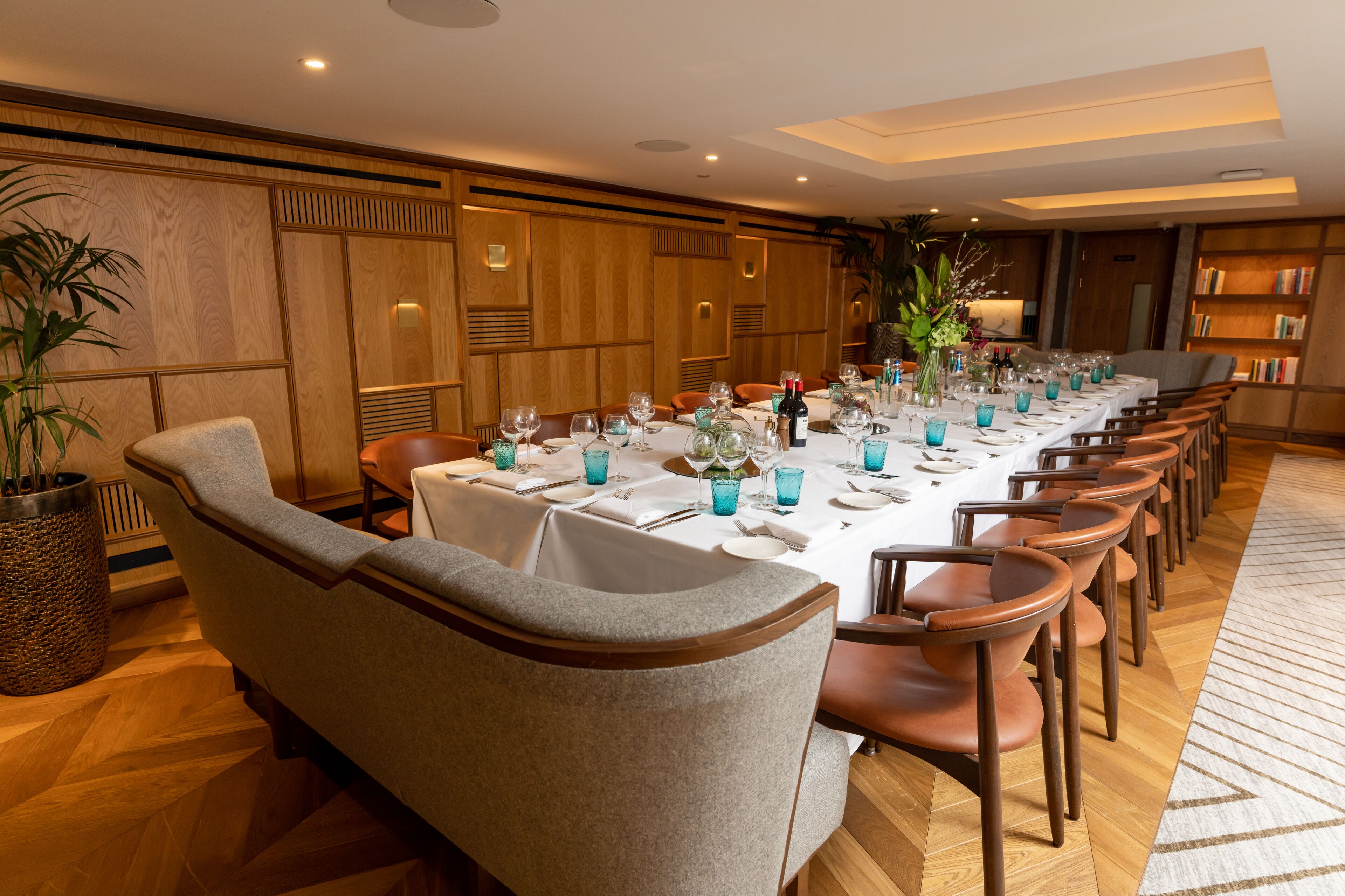 A long dining table set with blue glassware, surrounded by upholstered chairs.