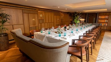 A long dining table set with blue glassware, surrounded by upholstered chairs.