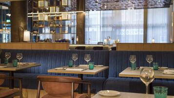 Um restaurante com cabines e mesas, algumas com almofadas azuis, e um espaço de bar ao fundo.