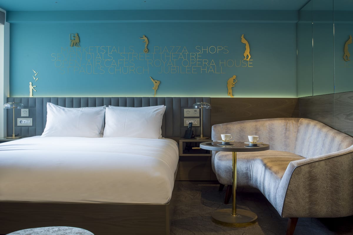 Een hotelkamer met een bed, een stoel, een tafeltje en een wand met decoratieve details.
