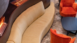 Et moderne loungeområde med en buet sofa og to livlige orange lænestole, en indbygget pejs samt en mørk trævæg.