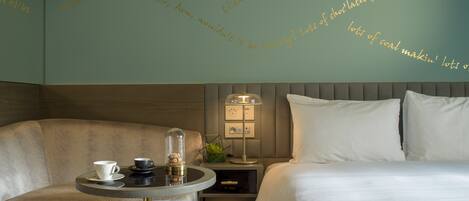 A hotel room with a bed, a chair, a table with a cup and saucer, and a lamp.