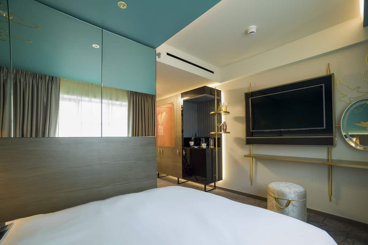 Een moderne hotelkamer met een groot bed, een aan de muur bevestigde televisie, een minibar en een inloopkast.