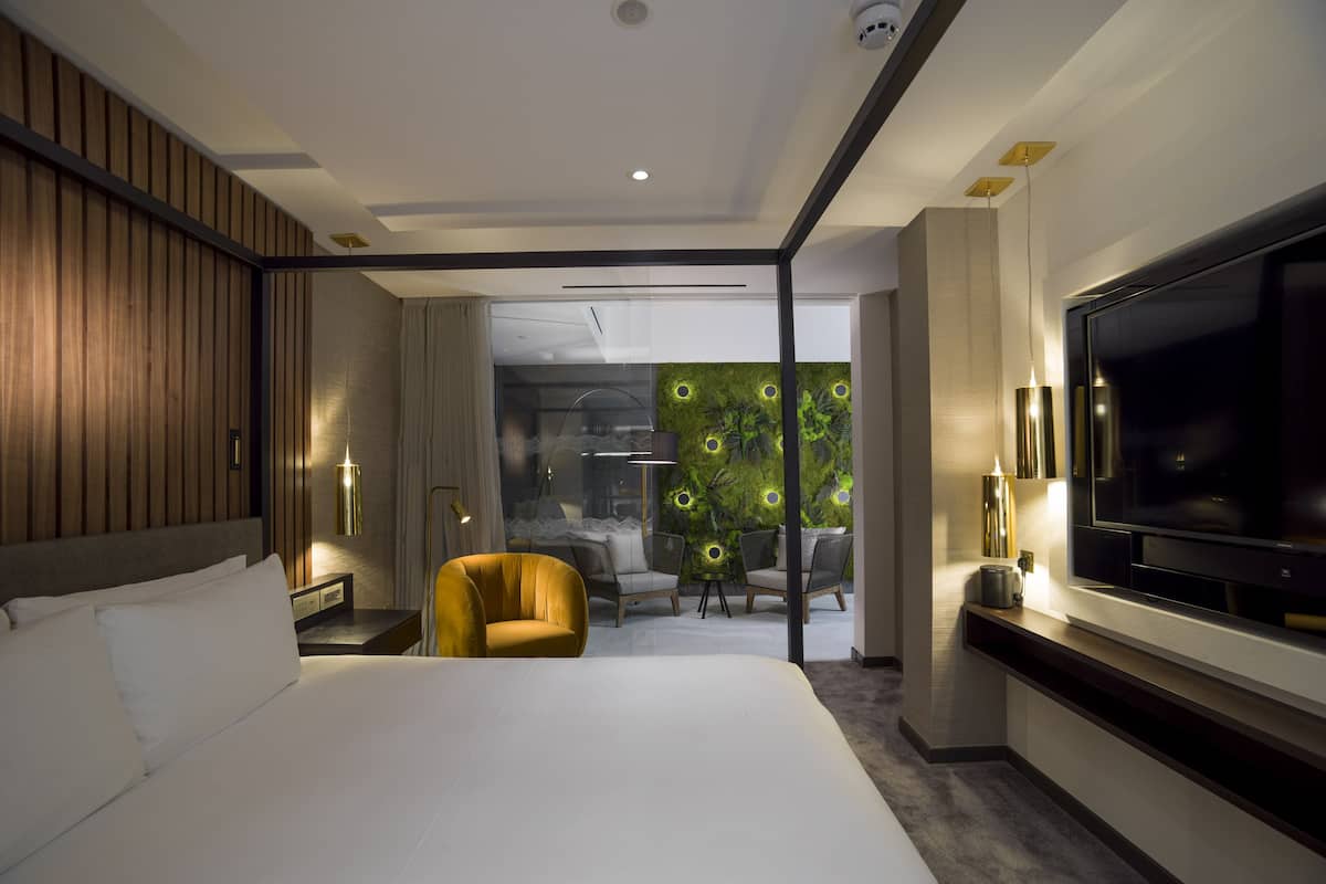 Een moderne hotelkamer met een groot bed, een flatscreen-tv, een zithoek met stoelen en een groene wand met ronde verlichting.