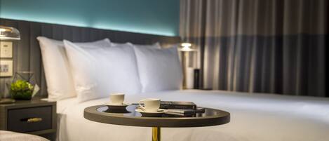 A neatly made bed with white linens, a bedside table with a cup and a book, and a wall with a geometric design.