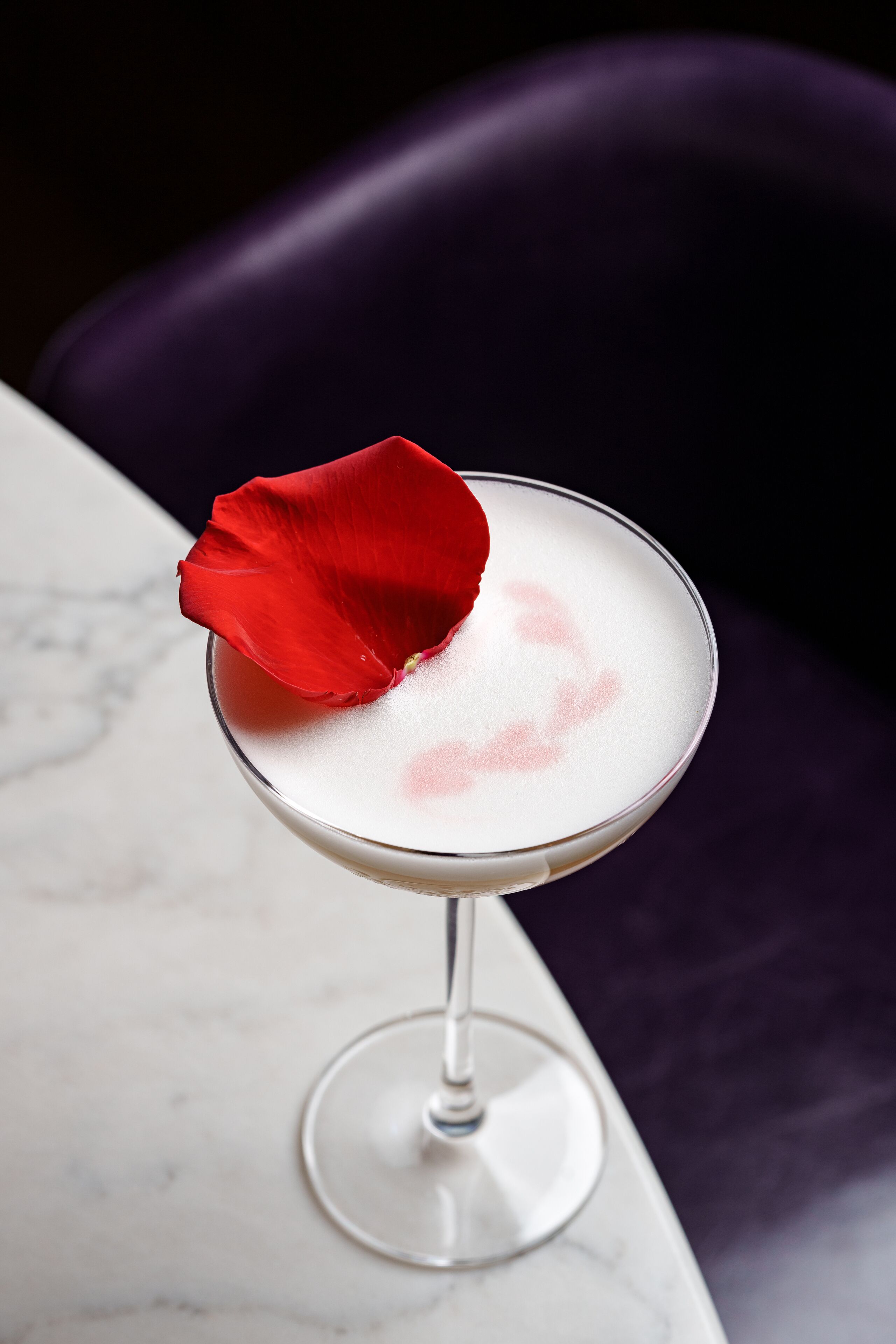 Een martini glas met een rode roos op de rand, op een marmeren oppervlak.