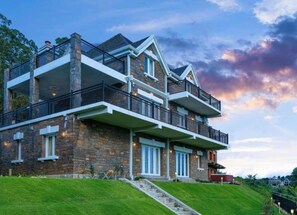 Un edificio de varios pisos de piedra con balcones, ventanas amplias y un césped bien cuidado.