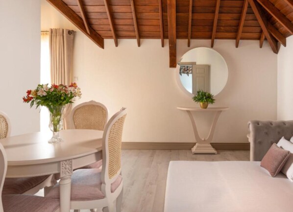 A room with a dining table, chairs, a round mirror, a sofa, and a bed.