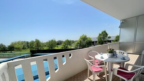 A balcony with a table and chairs, a potted plant, and a view of a green field and trees. - Spacious apartment just 200m from the sea (Porto Santa Margherita)
