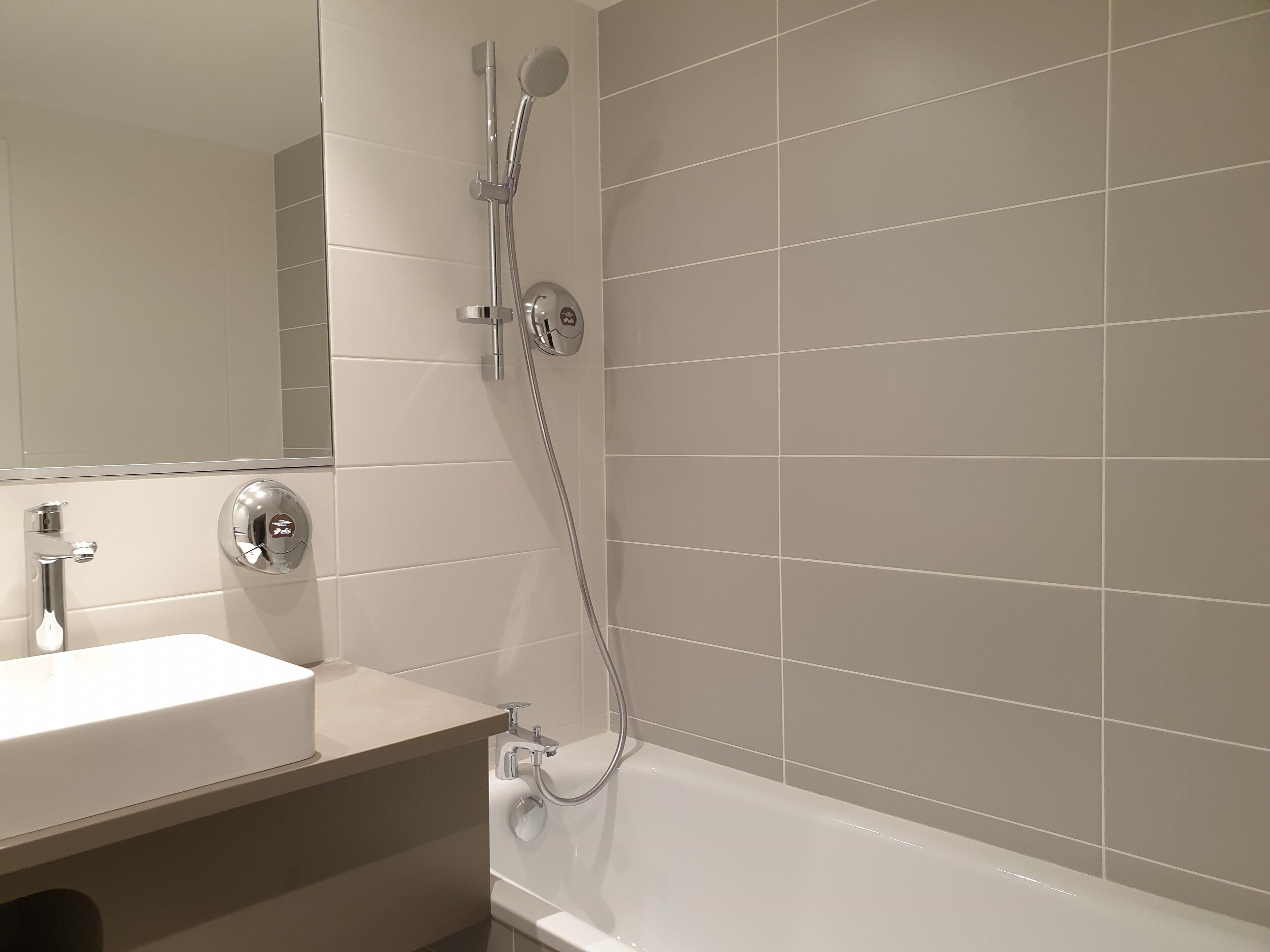 A modern bathroom with a white sink, a mirror, and a shower with a handheld showerhead.