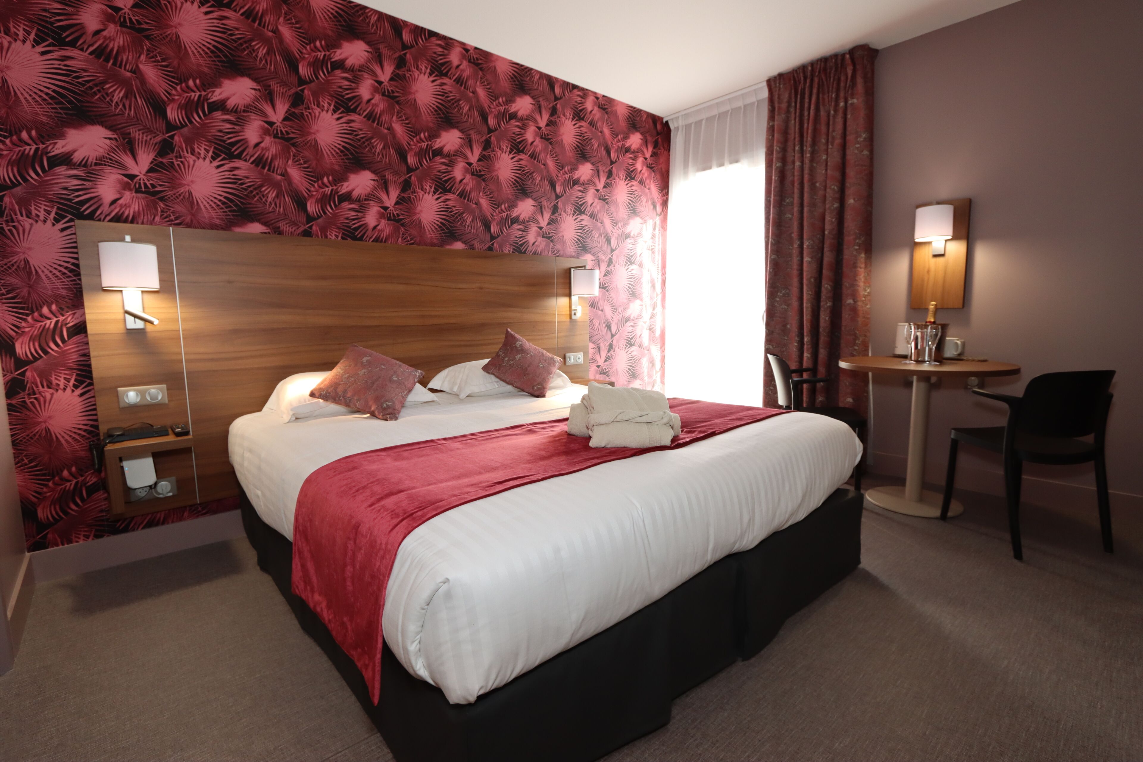 Une chambre d’hôtel avec un grand lit, un bureau, une chaise et une lampe fixée au mur.