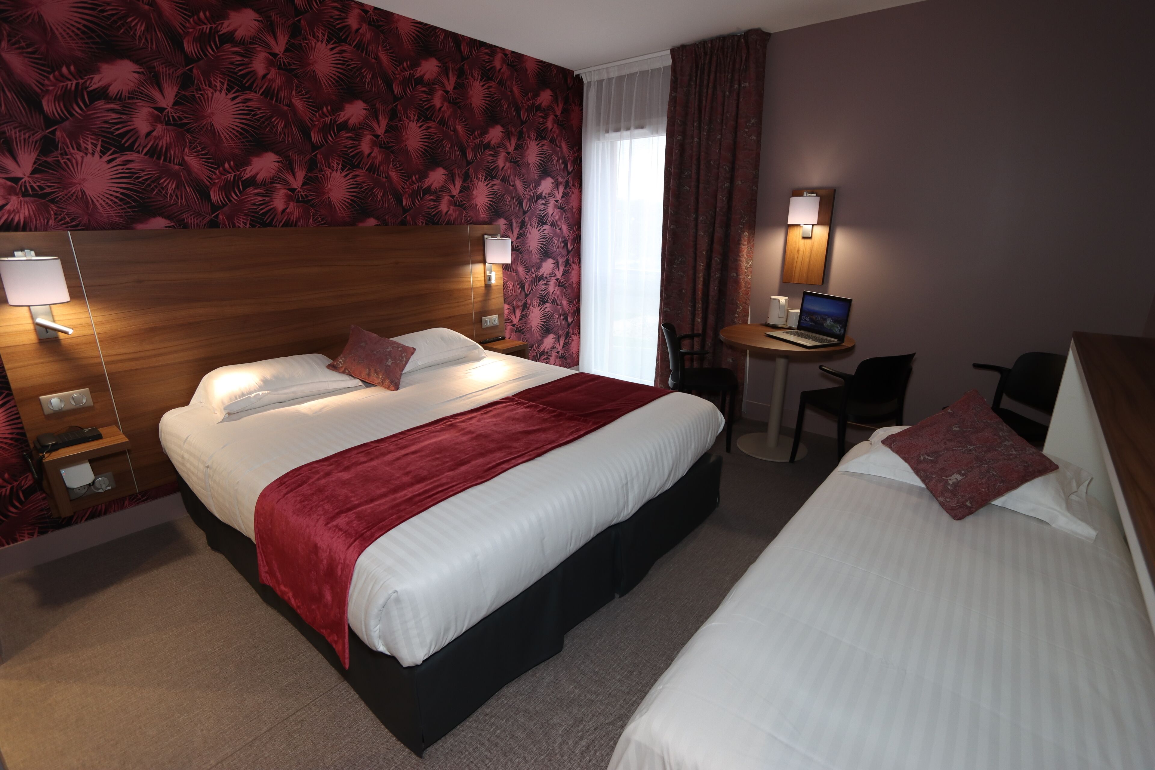 A hotel room with a large bed, a smaller bed, a desk with a laptop, and a chair.